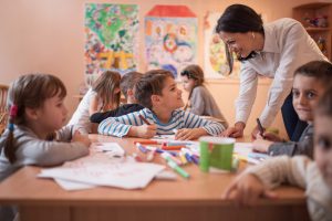 Happy female preschool teacher assisting little boy during a class in the classroom.
